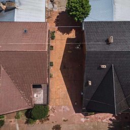 Fitter Tomasz Klupa - Widok z góry na dwa domy z dachami: jeden z brązową dachówką, drugi z czarną dachówką, oddzielone brukowanym podjazdem z cieniem drzewa.