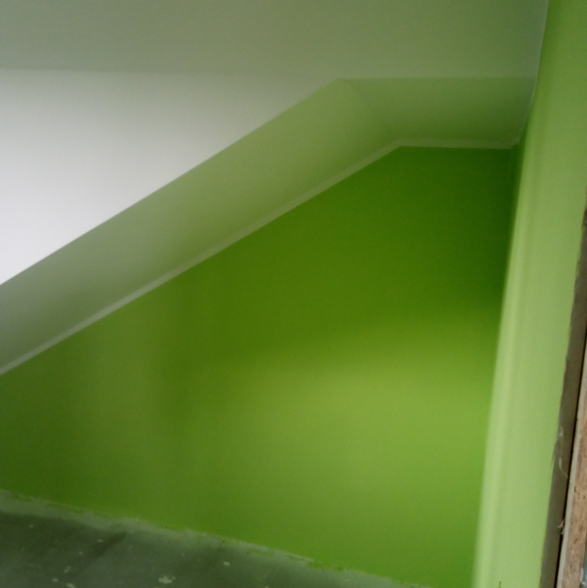 Świeżo pomalowana ściana w odcieniach zieleni, kontrastująca z białym sufitem pod skosem, widoczne niedociągnięcia malarskie przy podłodze i listwie sufitowej.