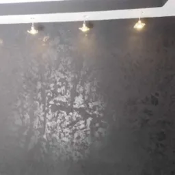 Szara ściana z dekoracyjną fakturą, oświetlona punktowymi lampami sufitowymi