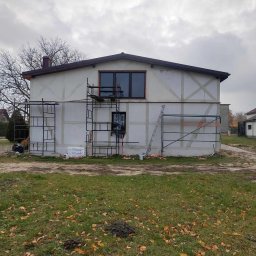 usługi ogólnobudowlane u Ilony - Dwupiętrowy dom w trakcie ocieplania, widoczne rusztowania, częściowo przyklejony styropian, przygotowany do dalszych prac wykończeniowych elewacji.
