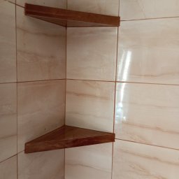 usługi ogólnobudowlane u Ilony - Dwie narożne, drewniane półki zamontowane w rogu łazienki wyłożonej beżowymi, marmurkowymi płytkami ceramicznymi.