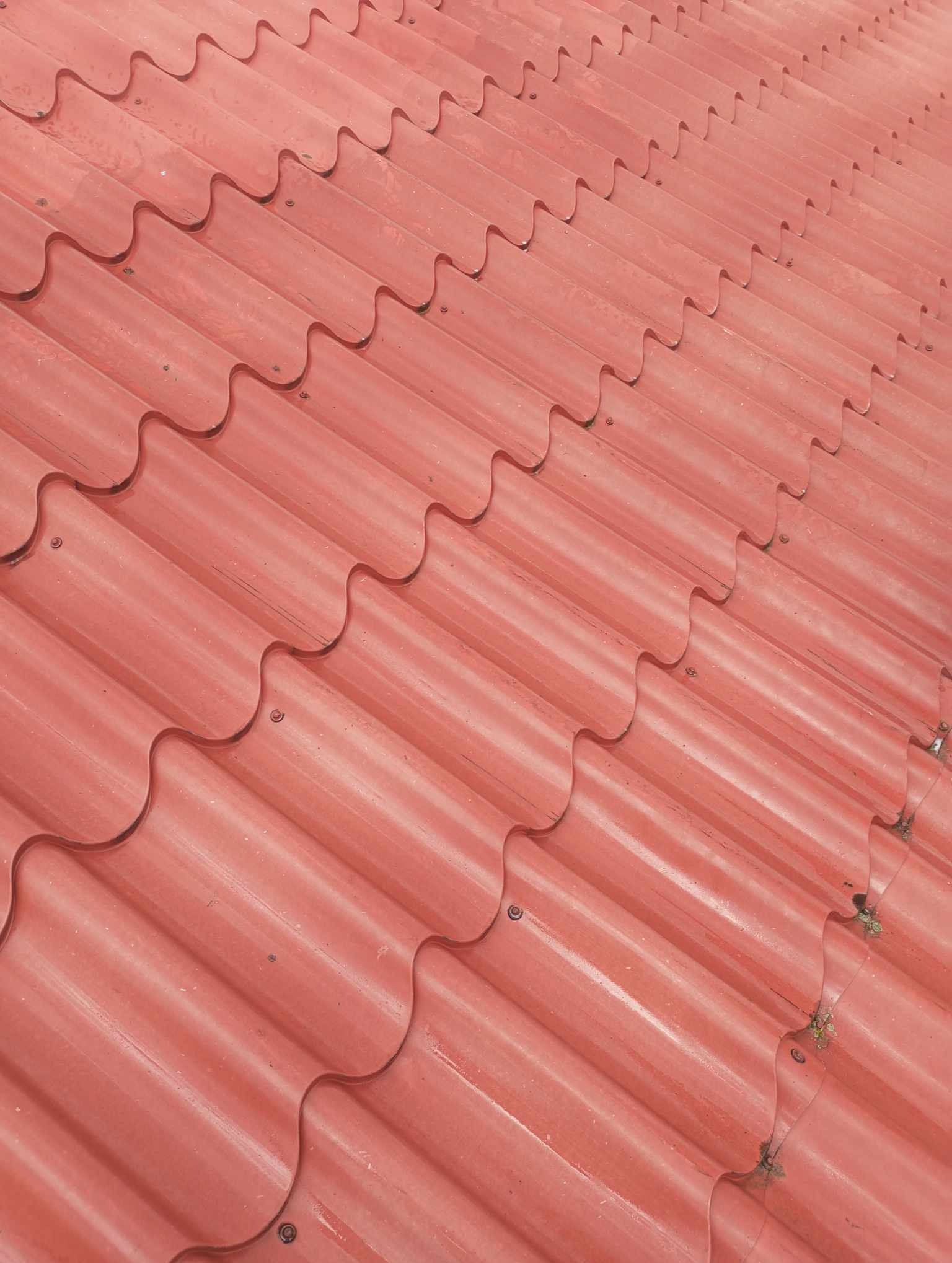 Czerwona blachodachówka falista, mocowana śrubami, widoczna z bliska pod kątem