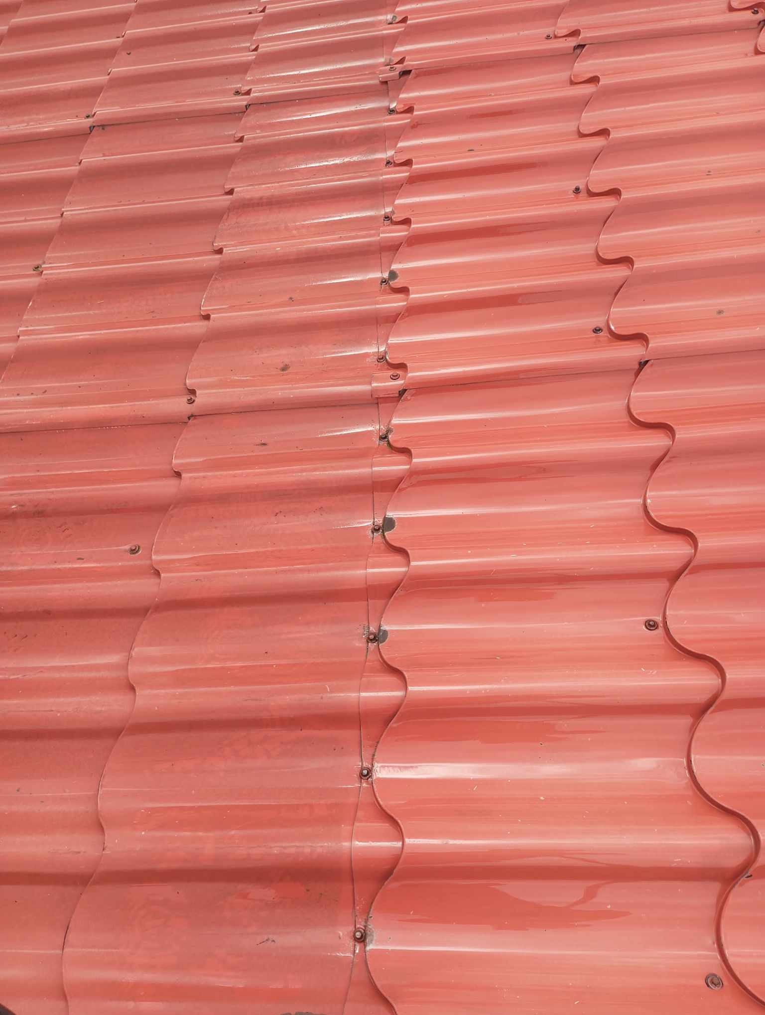 Czerwona blachodachówka na dachu, widoczne mocowania śrubowe i delikatne zarysowania na powierzchni.