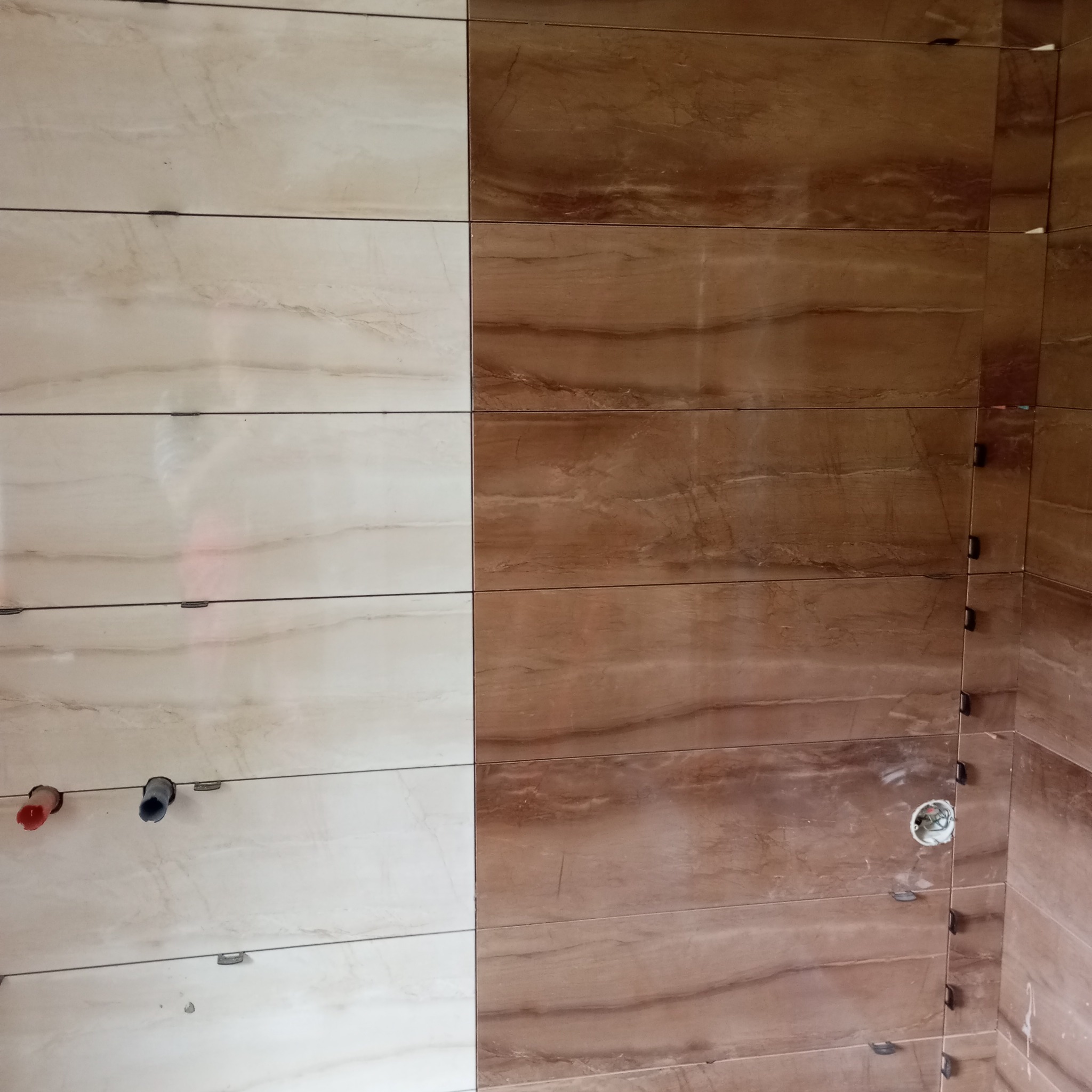 Układanie płytek imitujących marmur w łazience, widoczne krzyżyki dystansowe i wyprowadzenia instalacji wodnej.