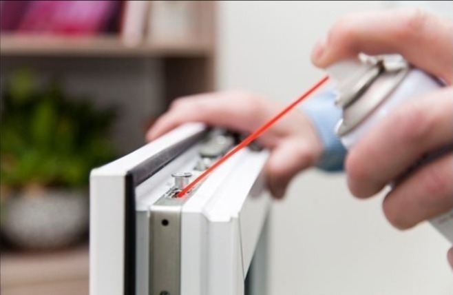 Konserwacja okna PCV: smarowanie mechanizmu okucia za pomocą aplikatora aerozolu z czerwoną słomką.