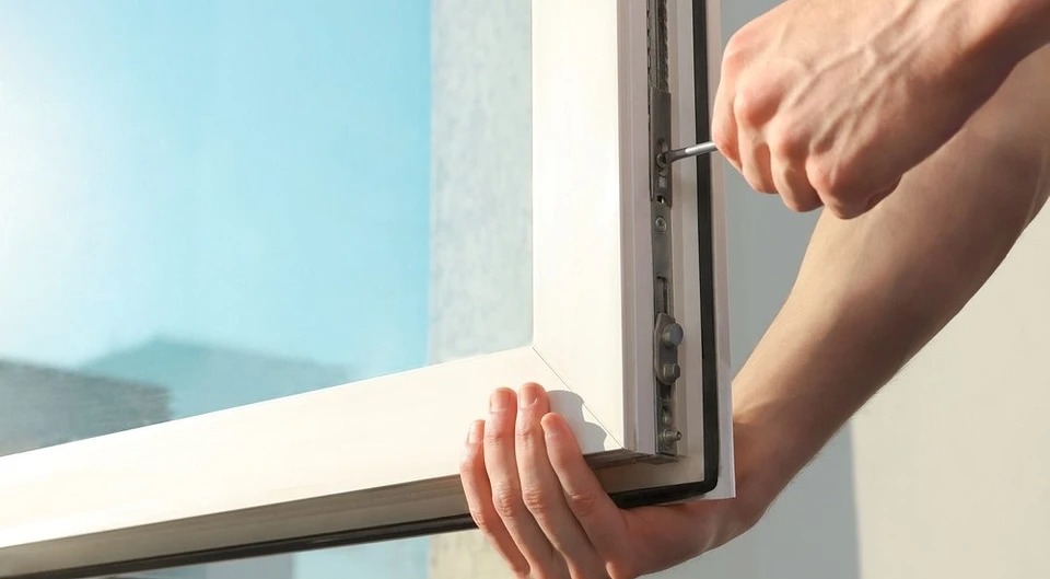 Regulacja okna PCV za pomocą śrubokręta, widoczny mechanizm okienny i dłoń montera.