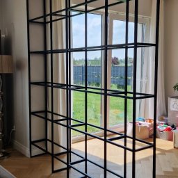 MASTER HOUSE - Metalowa konstrukcja w kształcie sześcianów, dzieląca przestrzeń w nowoczesnym wnętrzu z parkietem w jodełkę, widok na ogród przez okno balkonowe.