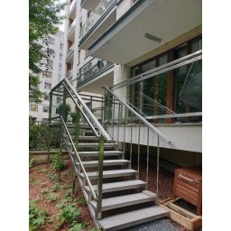 MASTER HOUSE - Zewnętrzne schody z metalową konstrukcją i szklaną balustradą prowadzące do balkonu w budynku mieszkalnym, otoczone zielenią.