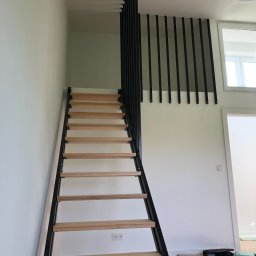 MASTER HOUSE - Nowoczesne schody z drewnianymi stopniami i czarną, metalową konstrukcją, widoczne z dołu, z minimalistyczną balustradą na antresoli i narzędziami na podłodze.