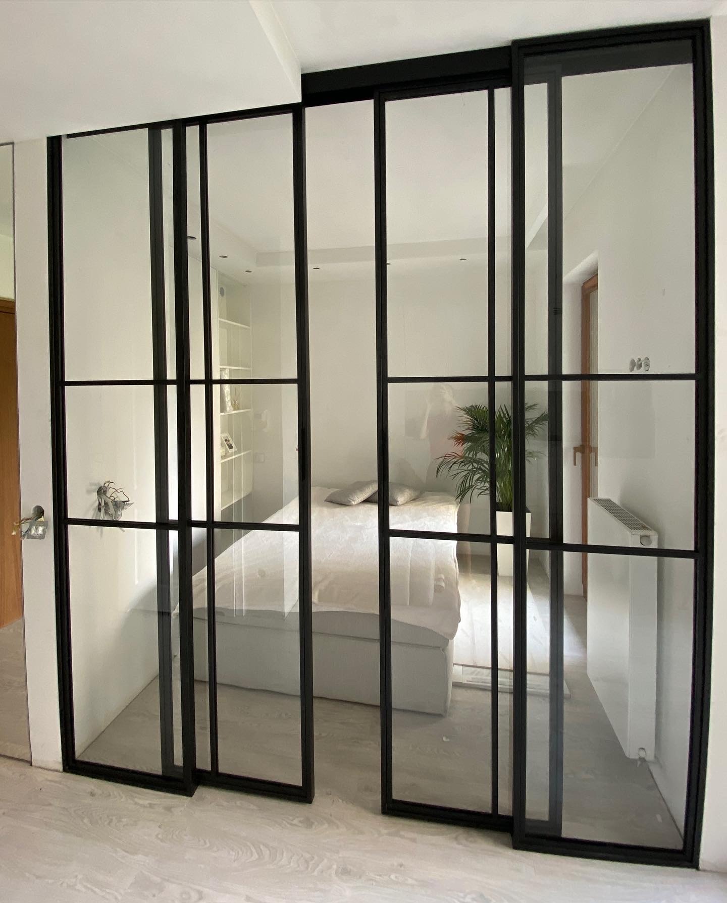 Przesuwne drzwi szklane z czarnymi szprosami, oddzielające sypialnię, zamontowane w domu w Nowej Wsi. Widoczne detale wykończenia podłogi i minimalistyczny wystrój wnętrza.