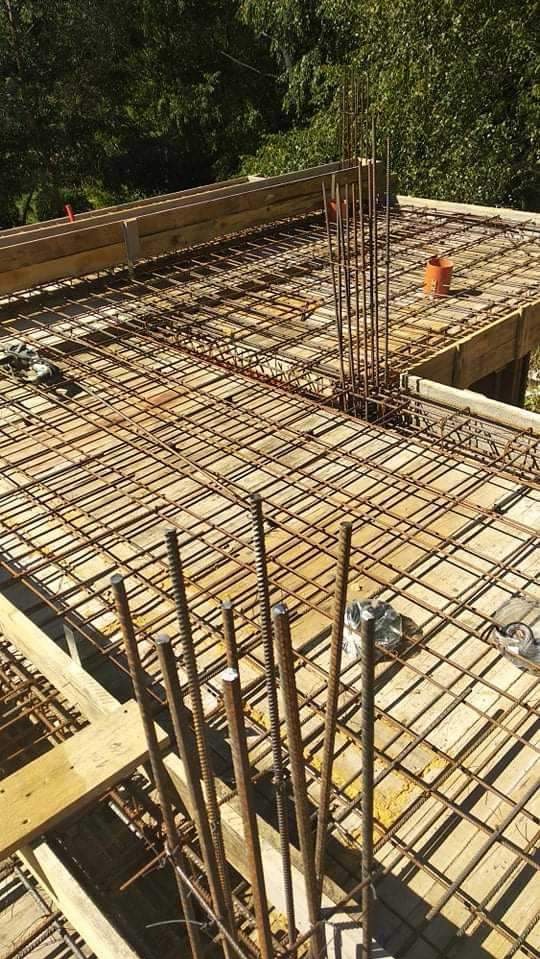 Zbrojenie płyty fundamentowej z wystającymi prętami pionowymi, widoczne deskowanie i elementy szalunku, etap budowy, widok z góry.