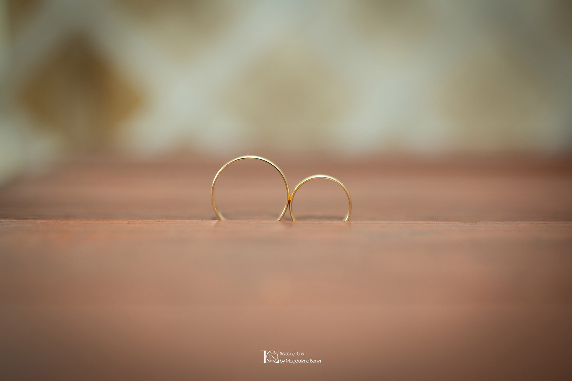 Dwa złote pierścionki ślubne ustawione pionowo na drewnianej powierzchni, z rozmytym tłem w ciepłych odcieniach.