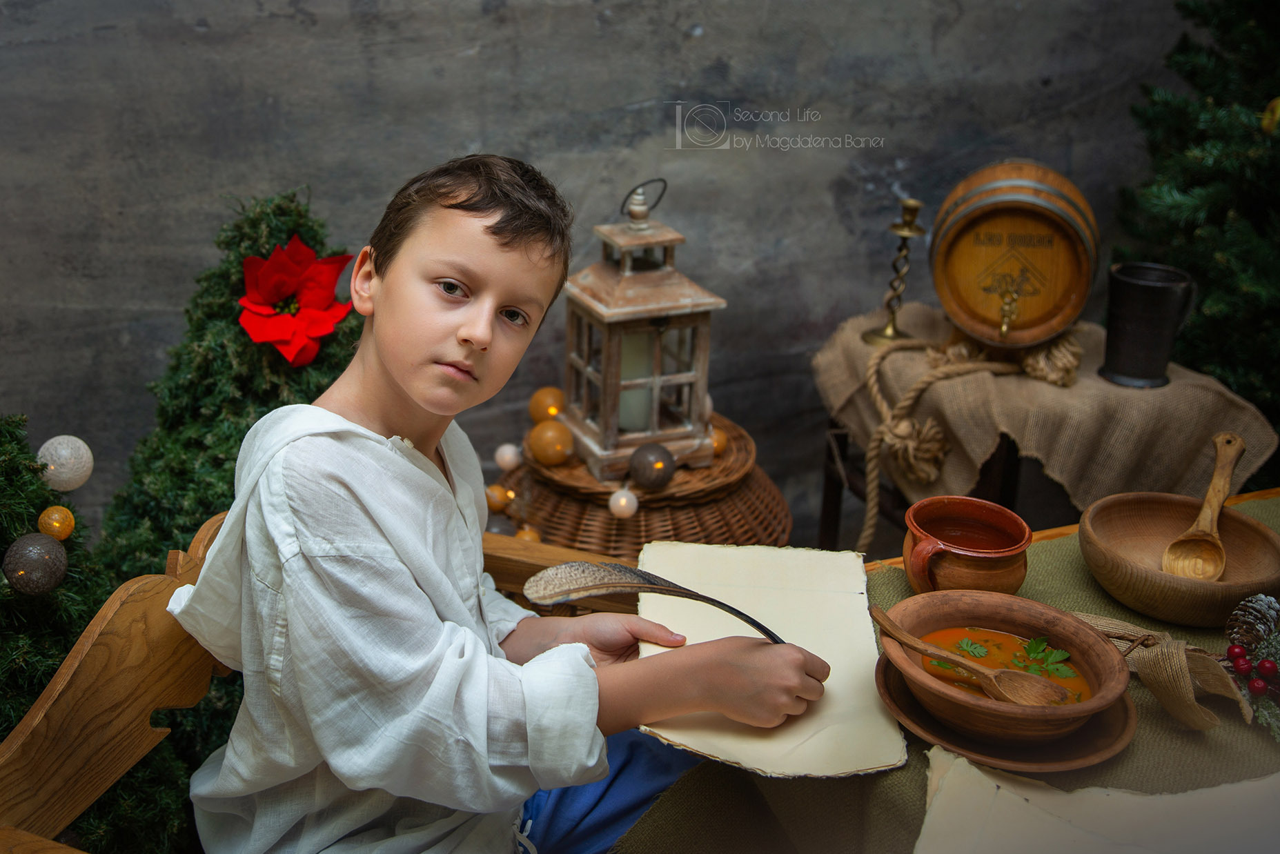 Stylizowana sesja szkolna: Chłopiec w białej koszuli pisze gęsim piórem na pergaminie, obok misa zupy, drewniane naczynia i dekoracje świąteczne.