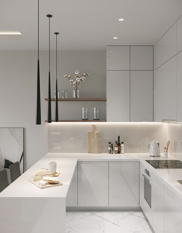 Nowoczesna, minimalistyczna kuchnia z białymi, błyszczącymi frontami, trzema długimi, czarnymi lampami wiszącymi i marmurową podłogą. Na blacie leżą drewniane deski do krojenia, przyprawy, czajnik...