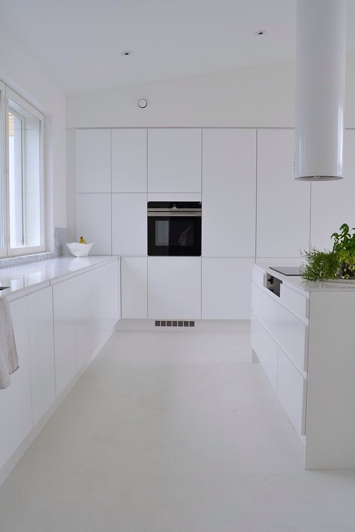 Minimalistyczna, całkowicie biała kuchnia z zabudową meblową bez uchwytów, wyspą kuchenną i okrągłym okapem cylindrycznym