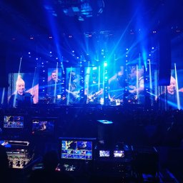 MRZ MARCIN RZEŹNICZEK - Koncert w Spodku: realizacja sygnału wideo na ekrany, widoczny mikser wideo i ekrany podglądowe, liczne reflektory sceniczne w kolorze niebieskim, publiczność w tle.