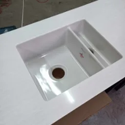 Biały blat kuchenny z wbudowanym, dwukomorowym zlewozmywakiem ceramicznym z okrągłym odpływem, widoczny fragment etykiety producenta.