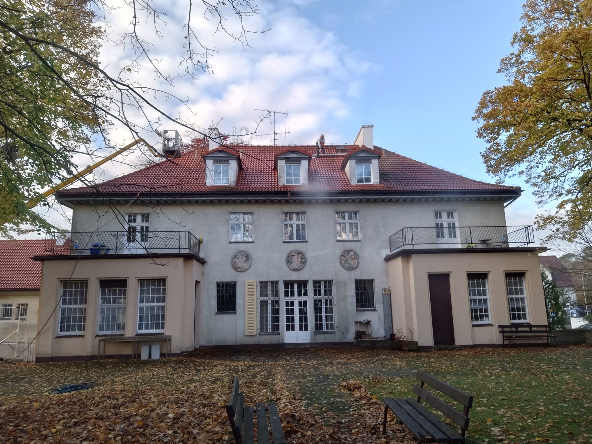 Prace na wysokościach w Wejherowie: Pracownik na podnośniku koszowym czyści dach budynku z czerwonej dachówki, unosząc parę wodną, widoczne trzy lukarny.