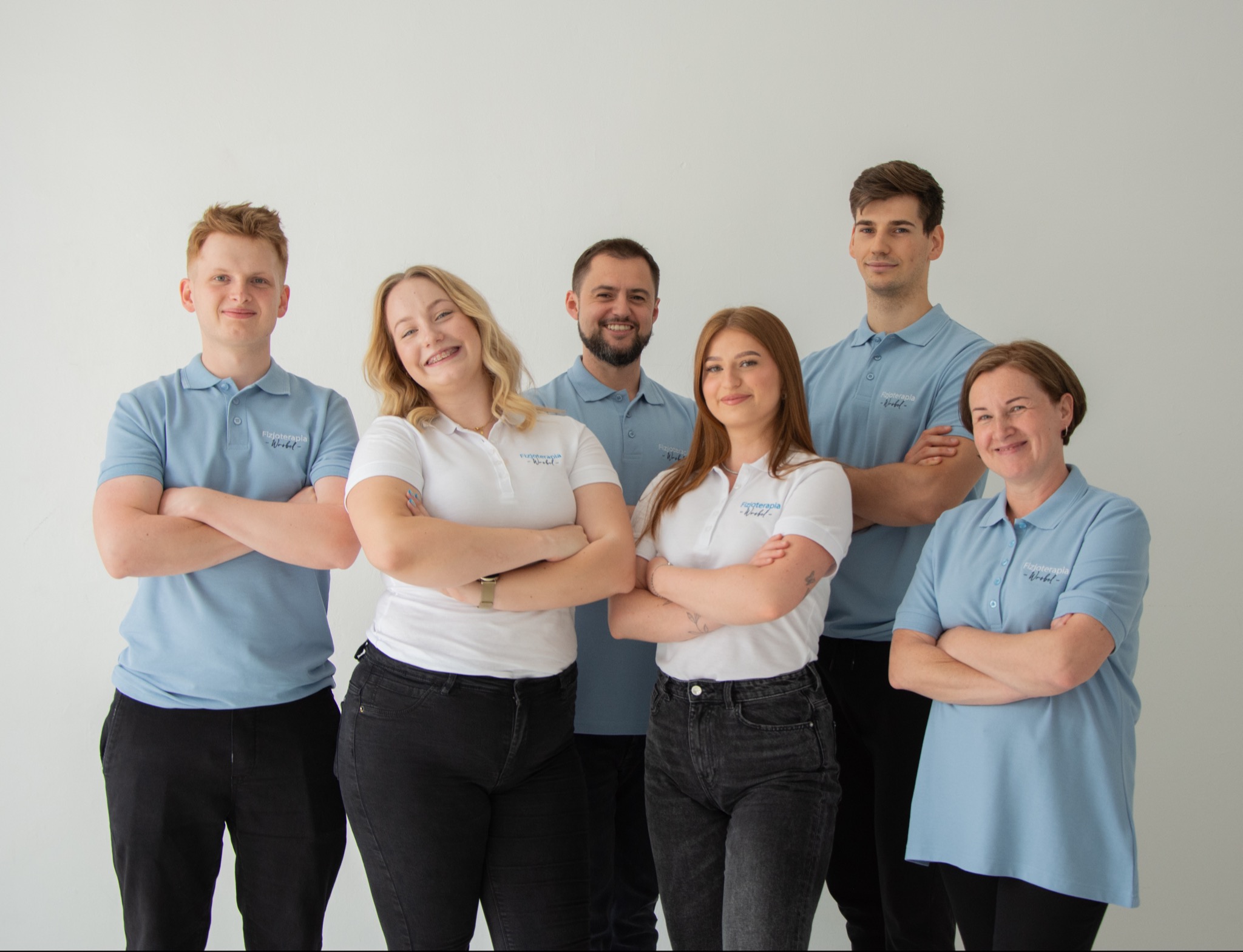 Zespół w ubraniach z logo firmy, pozujący na tle białej ściany, z uśmiechem prezentujący się jako grupa specjalistów.