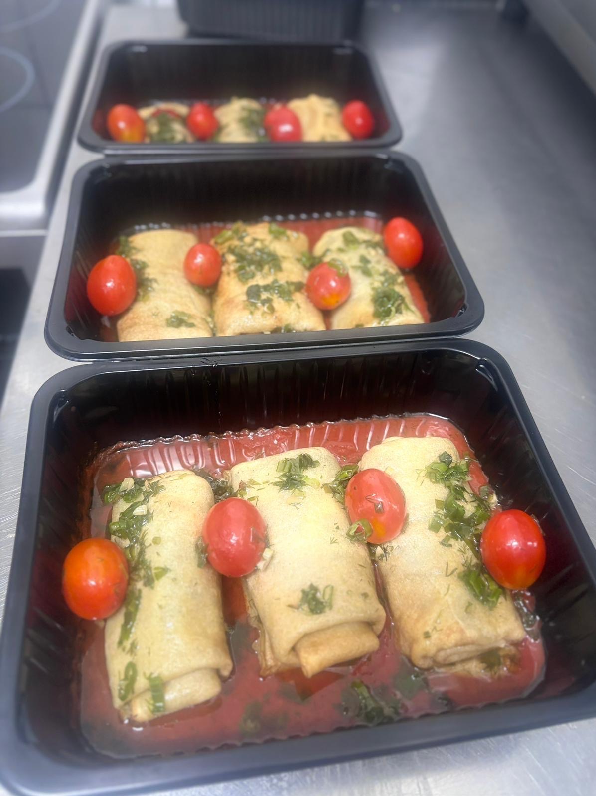 Catering dietetyczny: Naleśniki w sosie pomidorowym z ziołami i pomidorkami koktajlowymi, ułożone w czarnych tackach, gotowe do transportu.