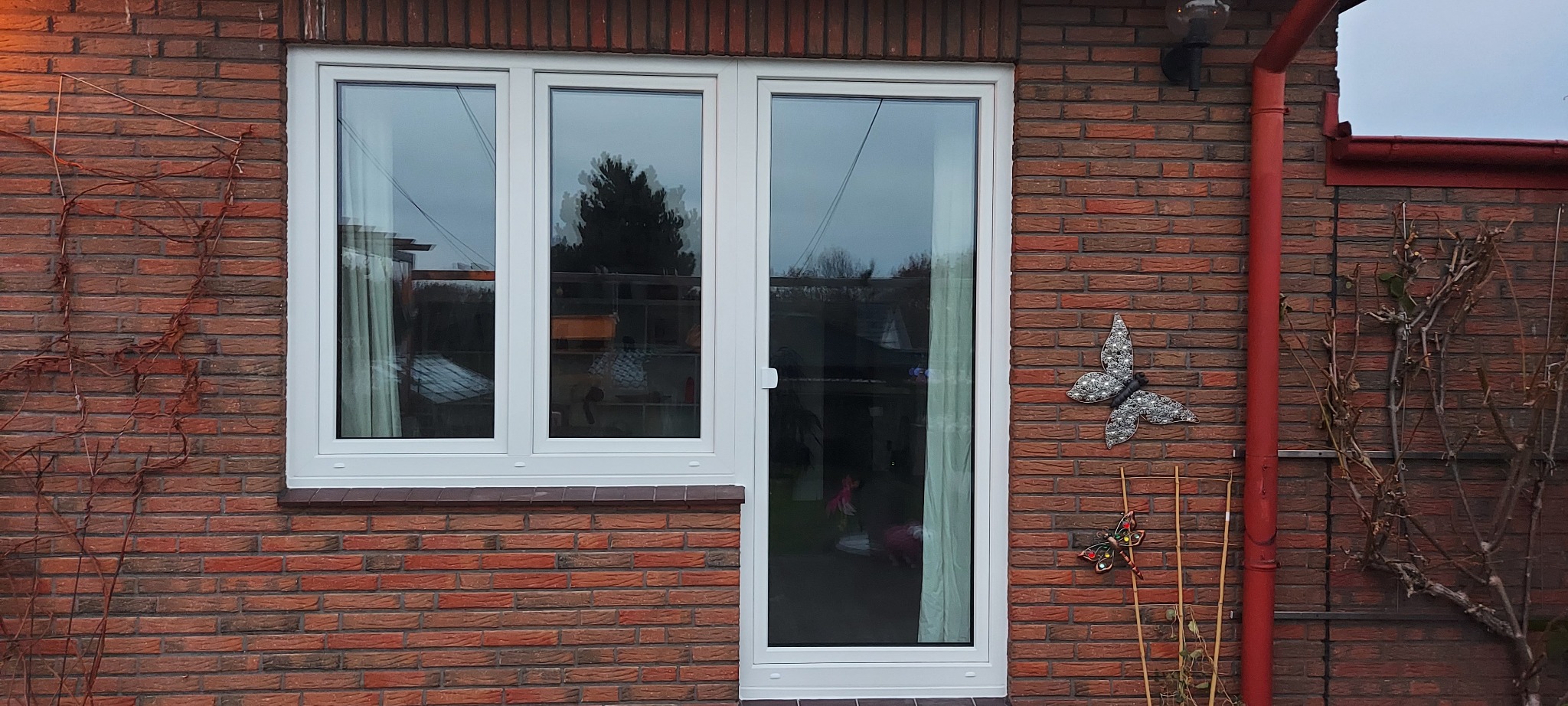 Nowe, białe okno z drzwiami balkonowymi w Rumi, zamontowane w ceglanym budynku, ozdobione dekoracjami w kształcie motyli.