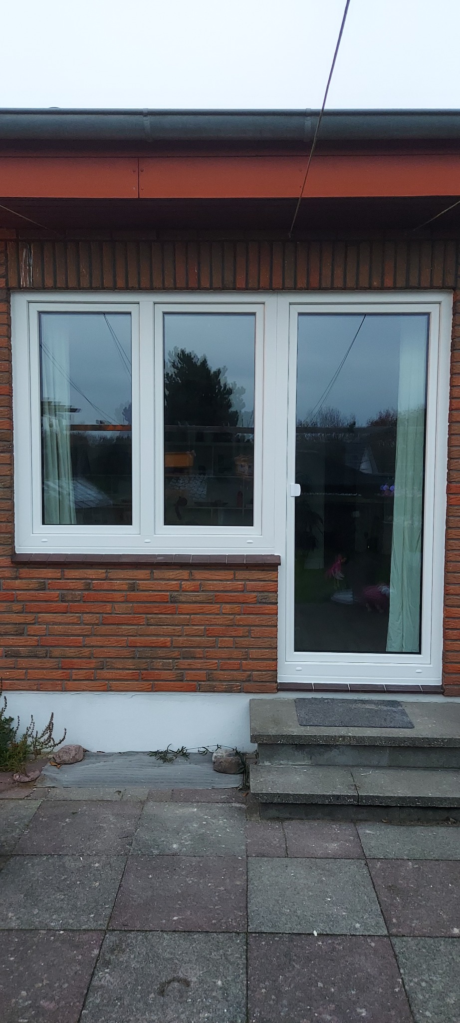 Białe okna i drzwi balkonowe w murze z czerwonej cegły, widok z zewnątrz na kamienny chodnik i schody.