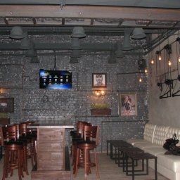 Andrii Chornyi - Industrialny bar z ciemną cegłą, widoczne rury instalacji elektrycznej na ścianie, telewizor z menu, oświetlenie w stylu loft i drewniane meble.