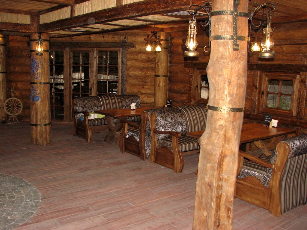 Rustykalne wnętrze restauracji z drewnianymi meblami, oświetlone lampami w stylu naftowym zawieszonymi na drewnianych kolumnach, tworzące ciepłą atmosferę.