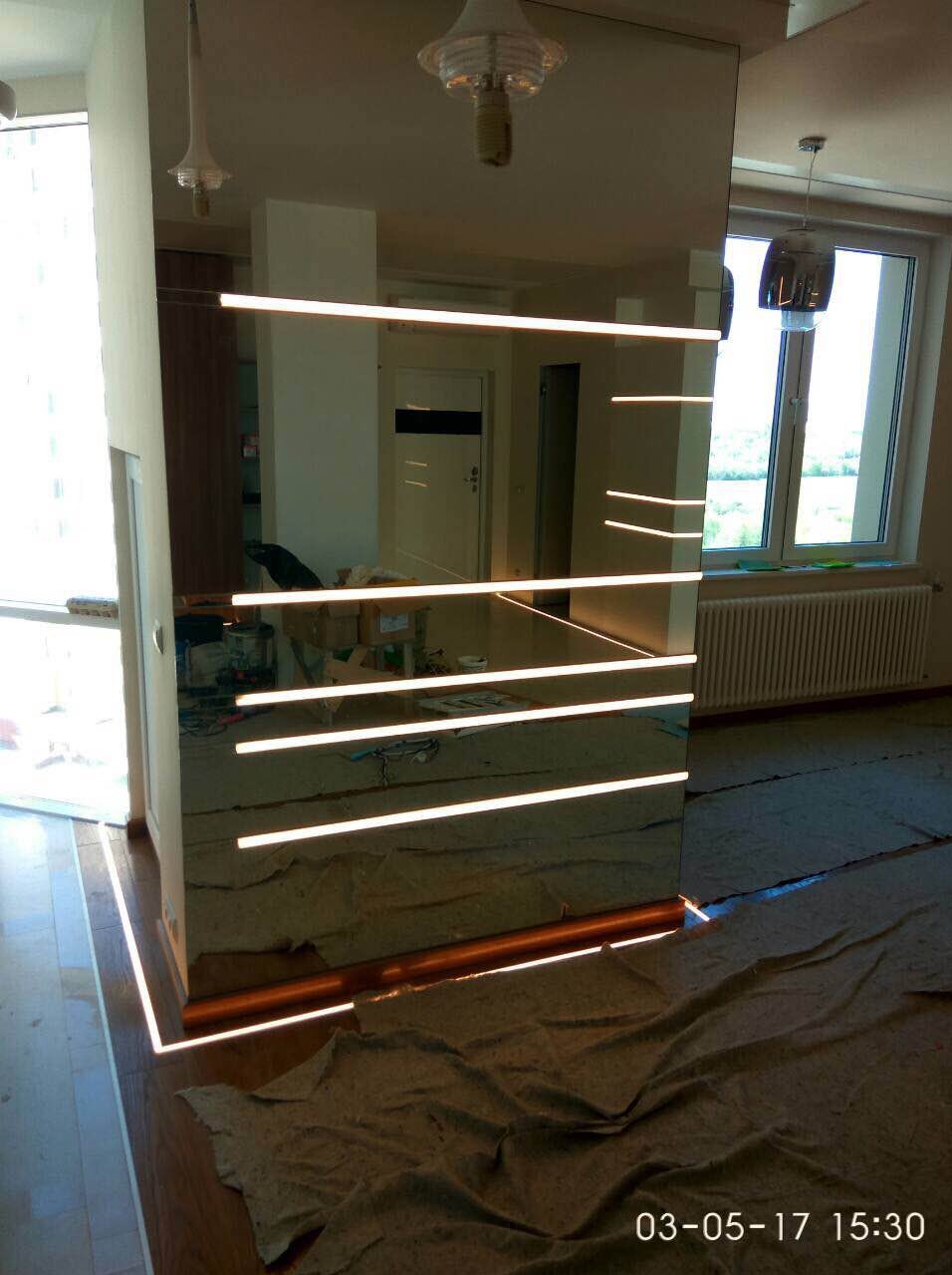 Szklana ściana z wbudowanym oświetleniem LED w trakcie montażu, widoczne narzędzia i zabezpieczenia na podłodze.