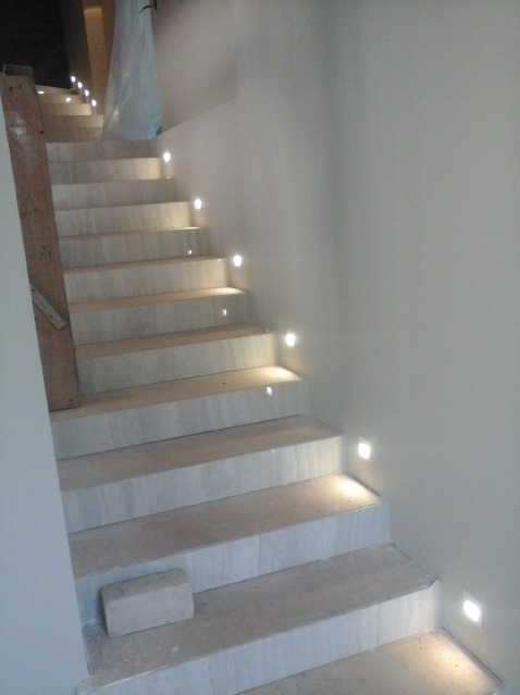 Wykończone marmurowe schody z zamontowanym oświetleniem punktowym LED w ścianie, widoczny fragment listwy przypodłogowej i fragment materiału zabezpieczającego na górze schodów.