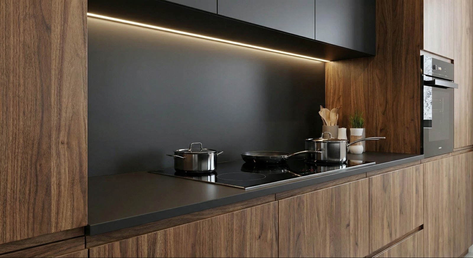 Nowoczesna kuchnia z drewnianymi frontami, czarnym panelem ściennym i oświetleniem LED. Na blacie garnki i patelnia na płycie indukcyjnej, obok piekarnik.