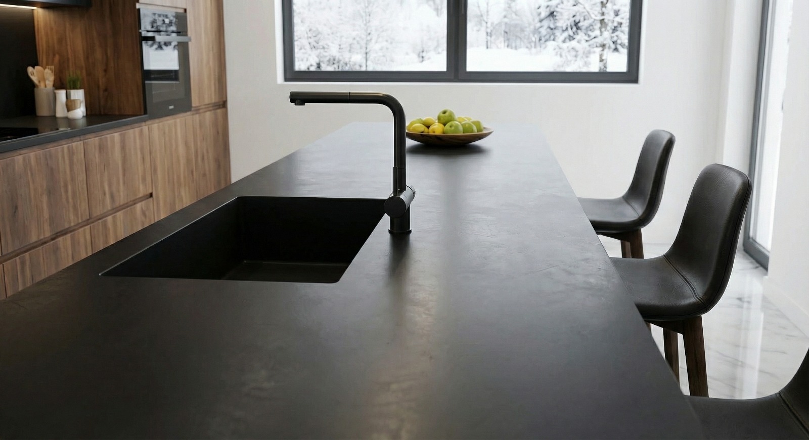 Nowoczesna kuchnia z czarnym, matowym blatem i zintegrowanym zlewem. Minimalistyczna bateria, drewniane szafki i widok na zimowy krajobraz za oknem.