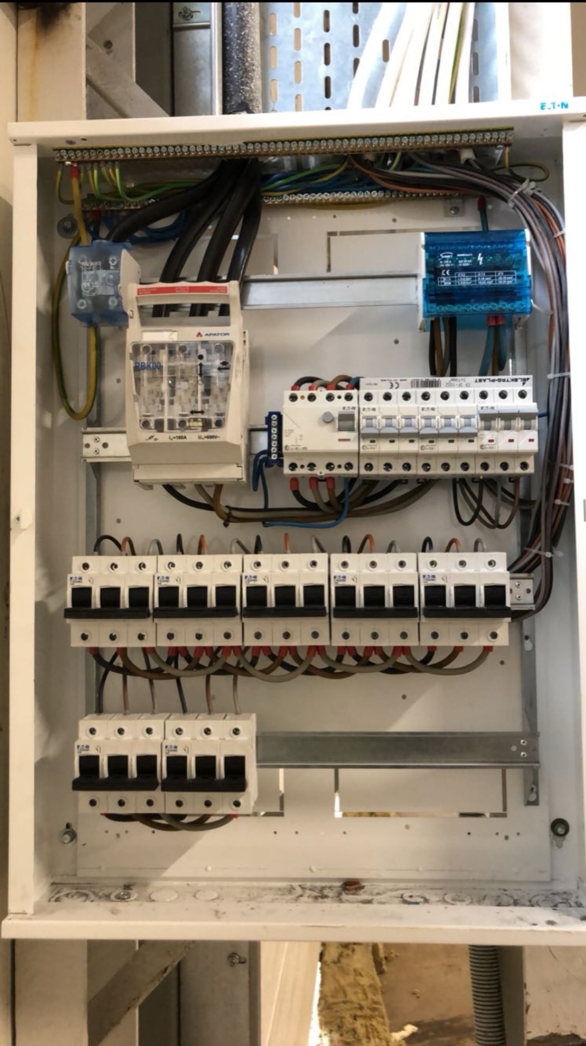 Rozdzielnia elektryczna w białej obudowie z widocznymi bezpiecznikami, przewodami i elementami montażowymi. Widok z bliska na zainstalowaną skrzynkę.