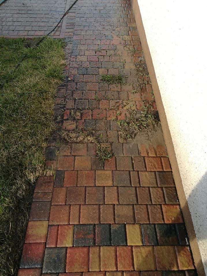 Częściowo umyta, wielobarwna kostka brukowa sąsiadująca z trawnikiem i ścianą. Widoczna różnica w czystości kostki, sugerująca etap mycia.