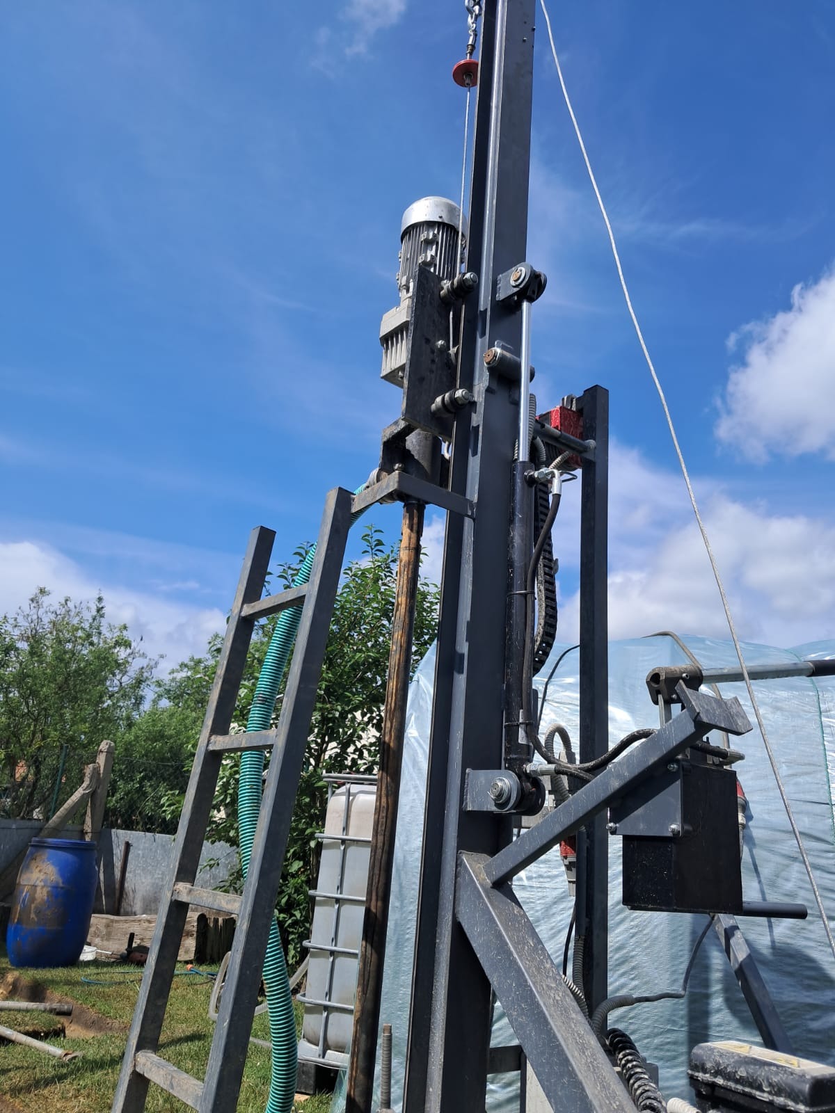 Wiertnica do studni głębinowych z silnikiem elektrycznym, drabina oparta o konstrukcję, błękitne niebo w tle.