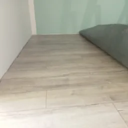 Jasne panele podłogowe ułożone w nowym pomieszczeniu z fragmentem zwiniętego dywanu w rogu