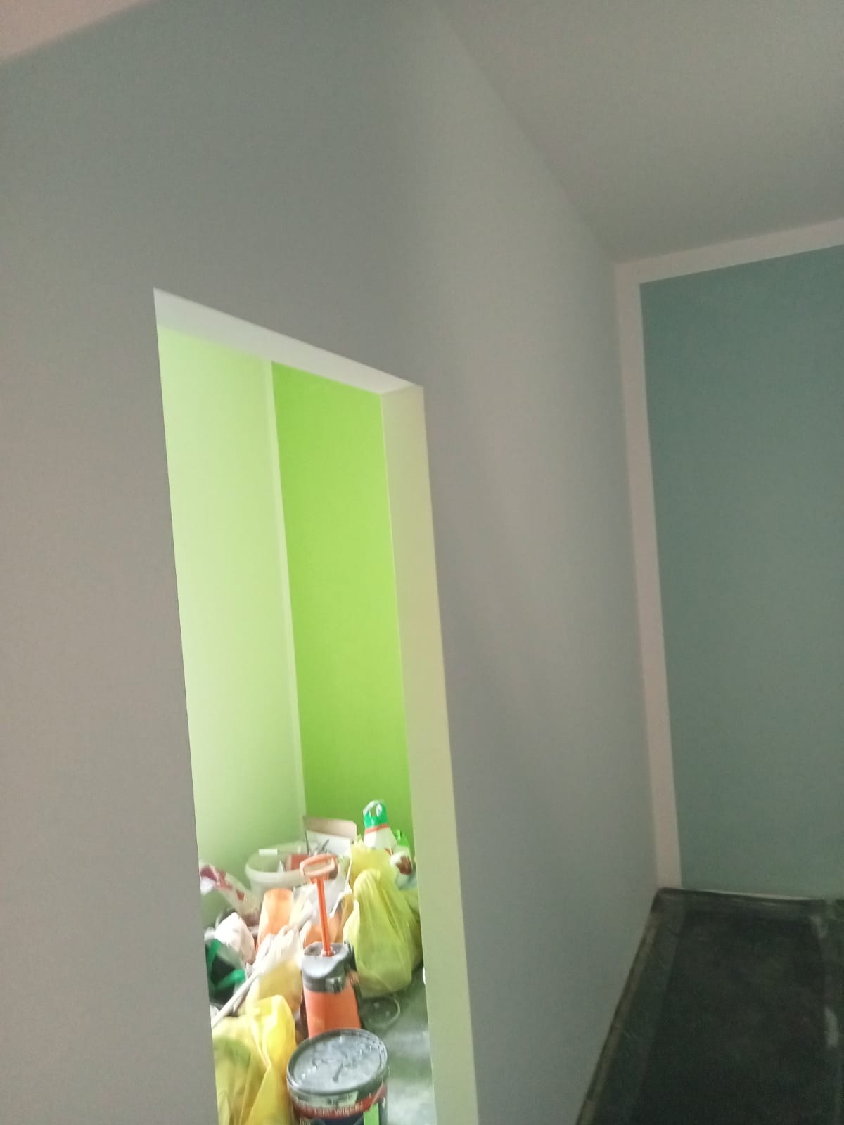 Pokój po malowaniu ścian na dwa kolory: szaro-niebieski i jaskrawozielony, widoczne narzędzia i materiały malarskie w drugim pomieszczeniu.