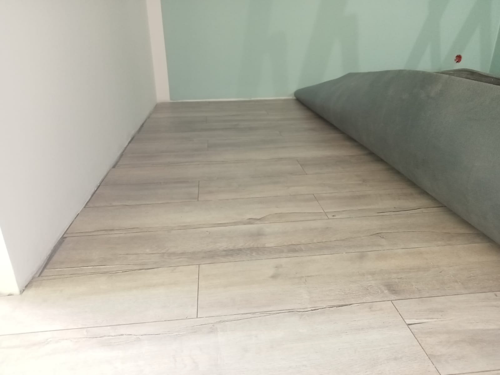 Jasne panele podłogowe ułożone w nowym pomieszczeniu z fragmentem zwiniętego dywanu w rogu