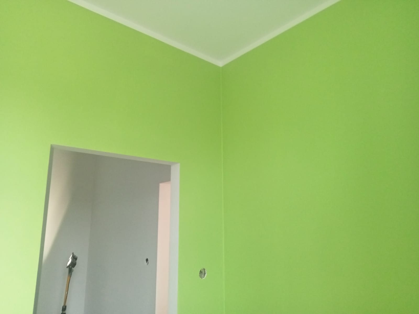 Ściana w odcieniu świeżej zieleni w Świdnicy, pomalowana z precyzją, widoczny fragment sufitu z listwą oraz wejście do pomieszczenia w trakcie prac wykończeniowych.