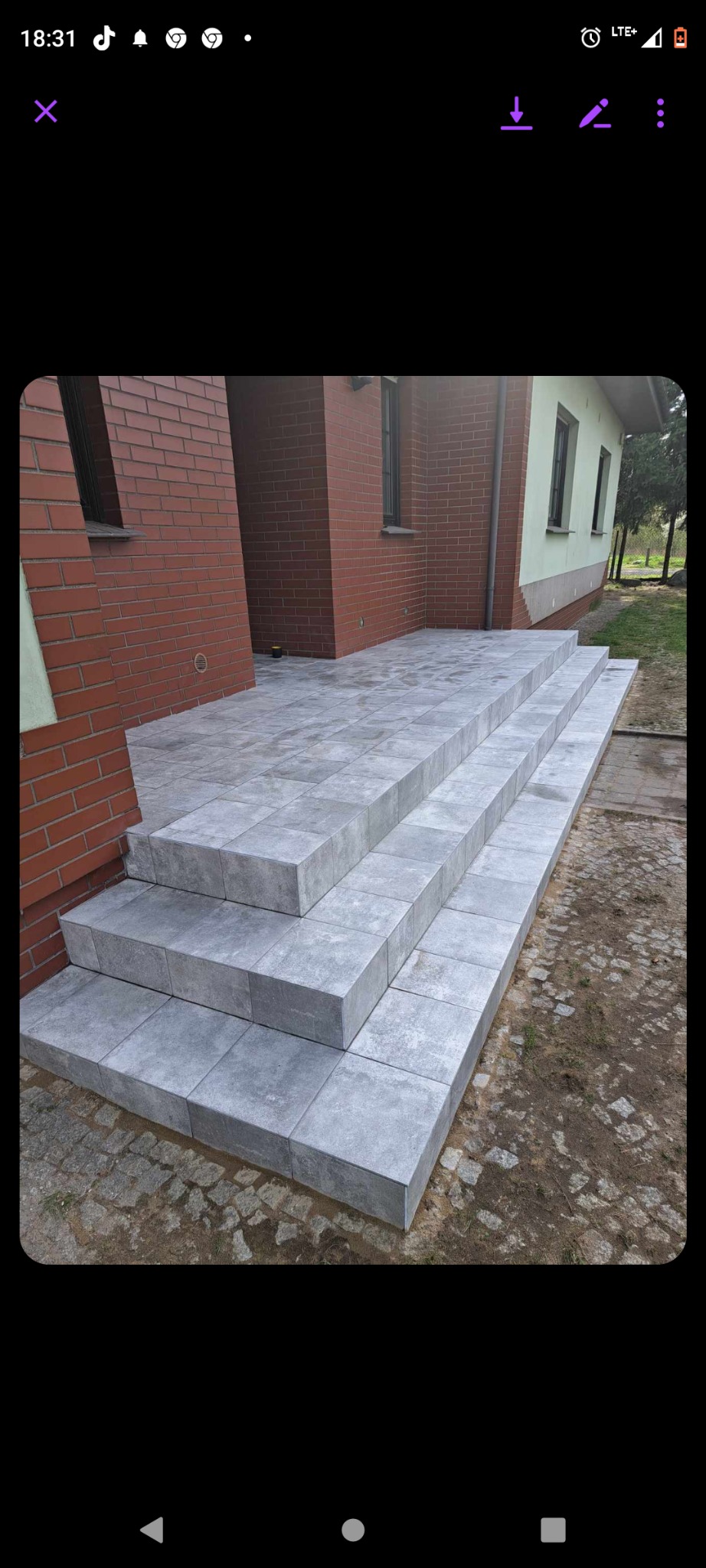 Schody wejściowe do domu wyłożone szarą kostką brukową, widok z dołu, ceglana elewacja budynku w tle.