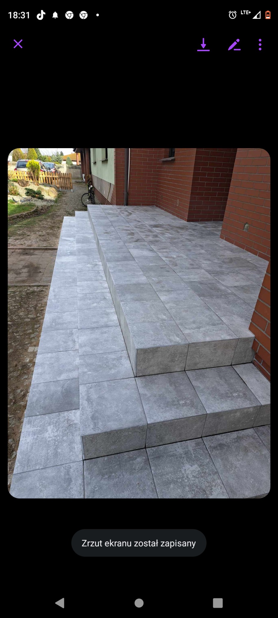 Wykończony taras z szarych, betonowych płyt na schodach wejściowych do domu z cegły.