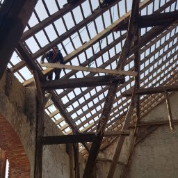 REMS & STEL DYNAMICS - Demontaż starej więźby dachowej z widocznymi elementami muru z cegły i pracownikami na konstrukcji.