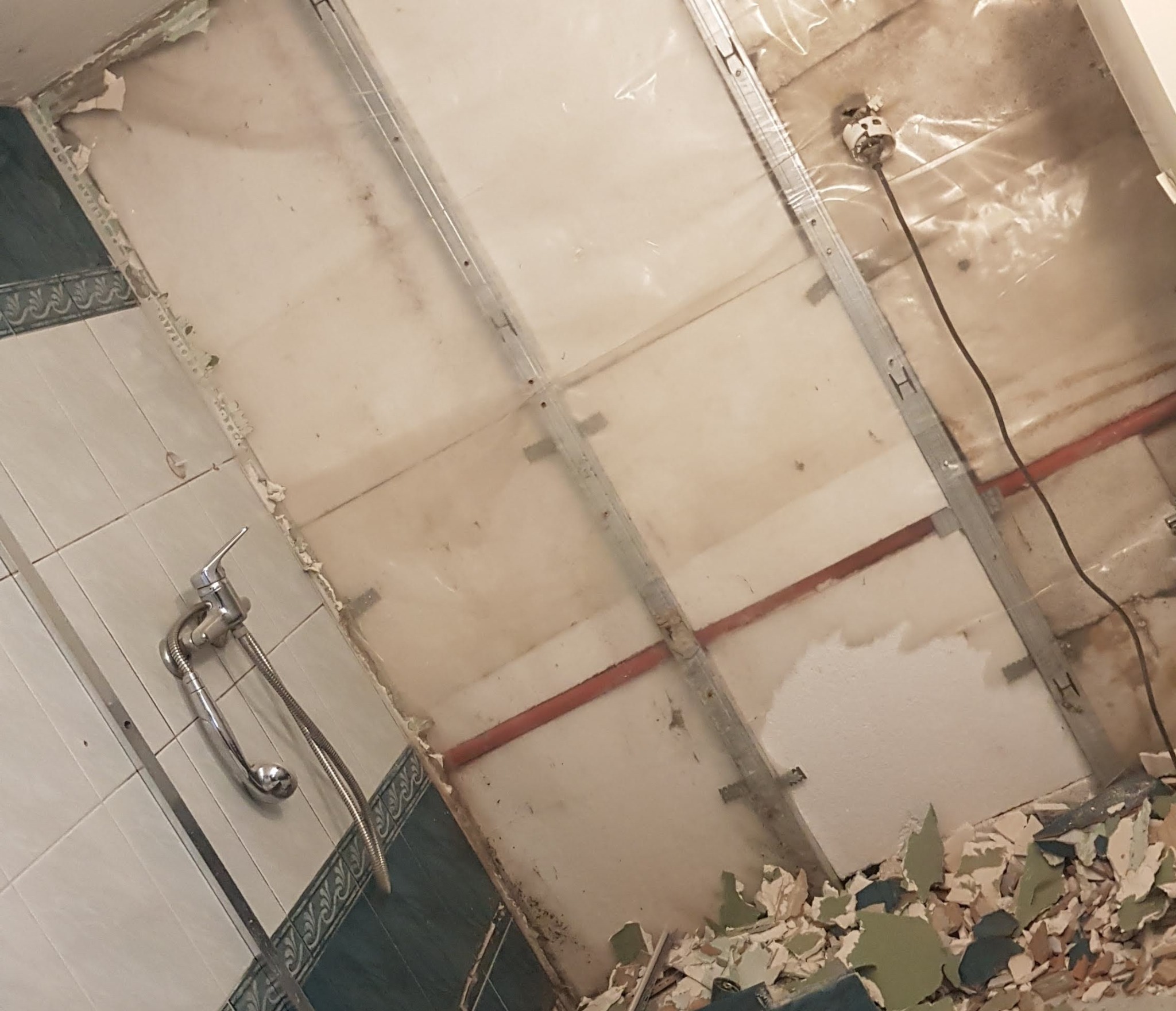 Demontaż sufitu w łazience z widocznymi elementami konstrukcyjnymi, instalacją elektryczną i gruzem po demontażu.