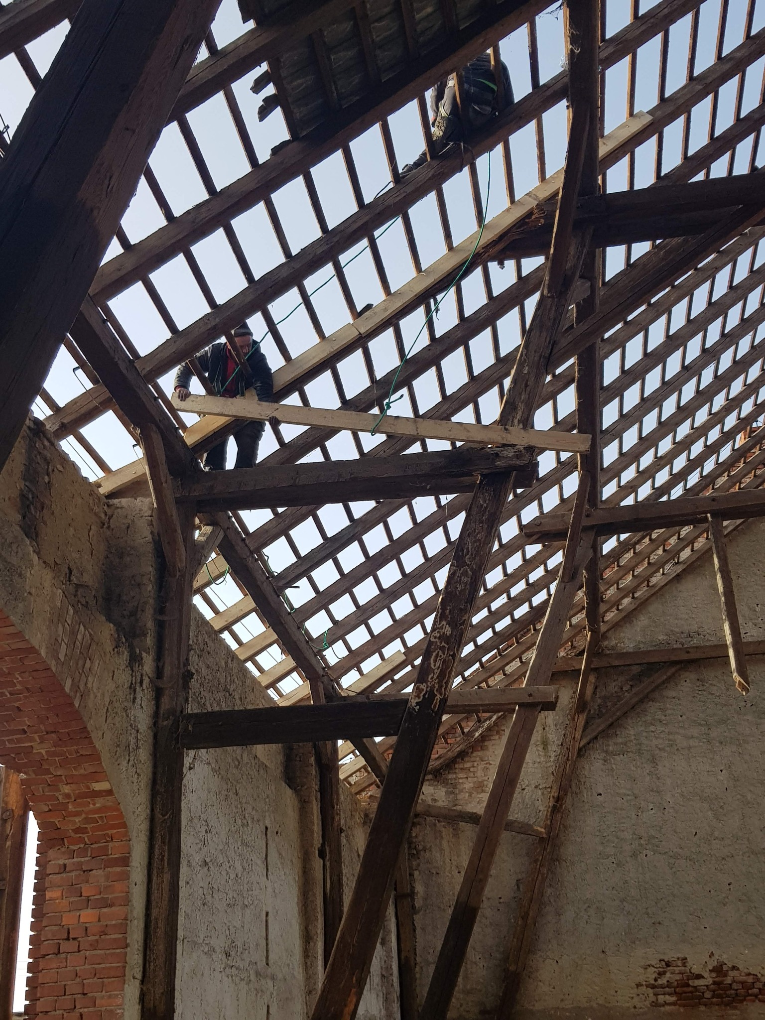 Demontaż starej więźby dachowej z widocznymi elementami muru z cegły i pracownikami na konstrukcji.