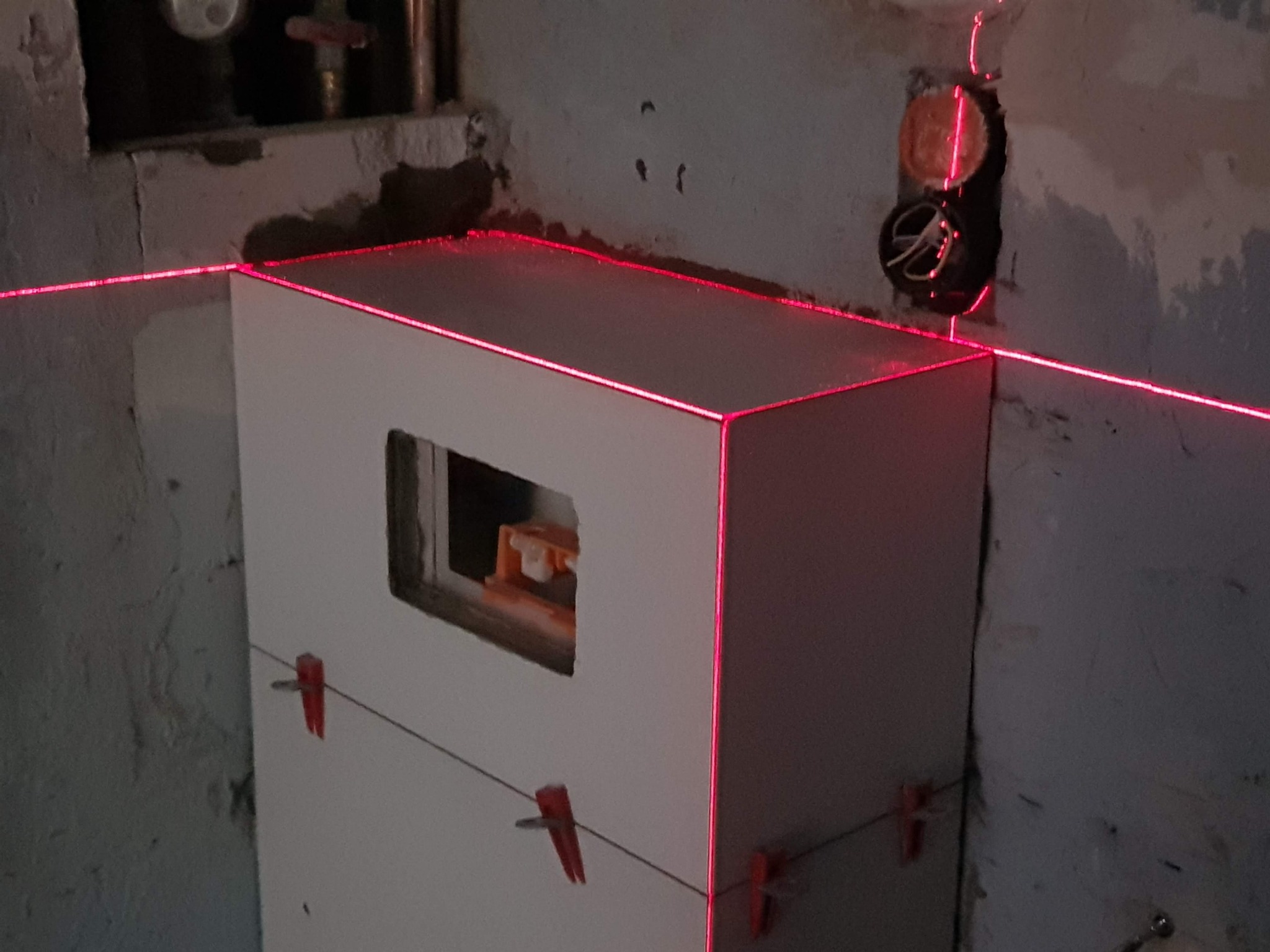 Biała zabudowa geberit z otworem rewizyjnym, poziomowana laserem krzyżowym i stabilizowana sznurkiem z klamerkami, na tle surowej ściany w łazience w trakcie remontu.