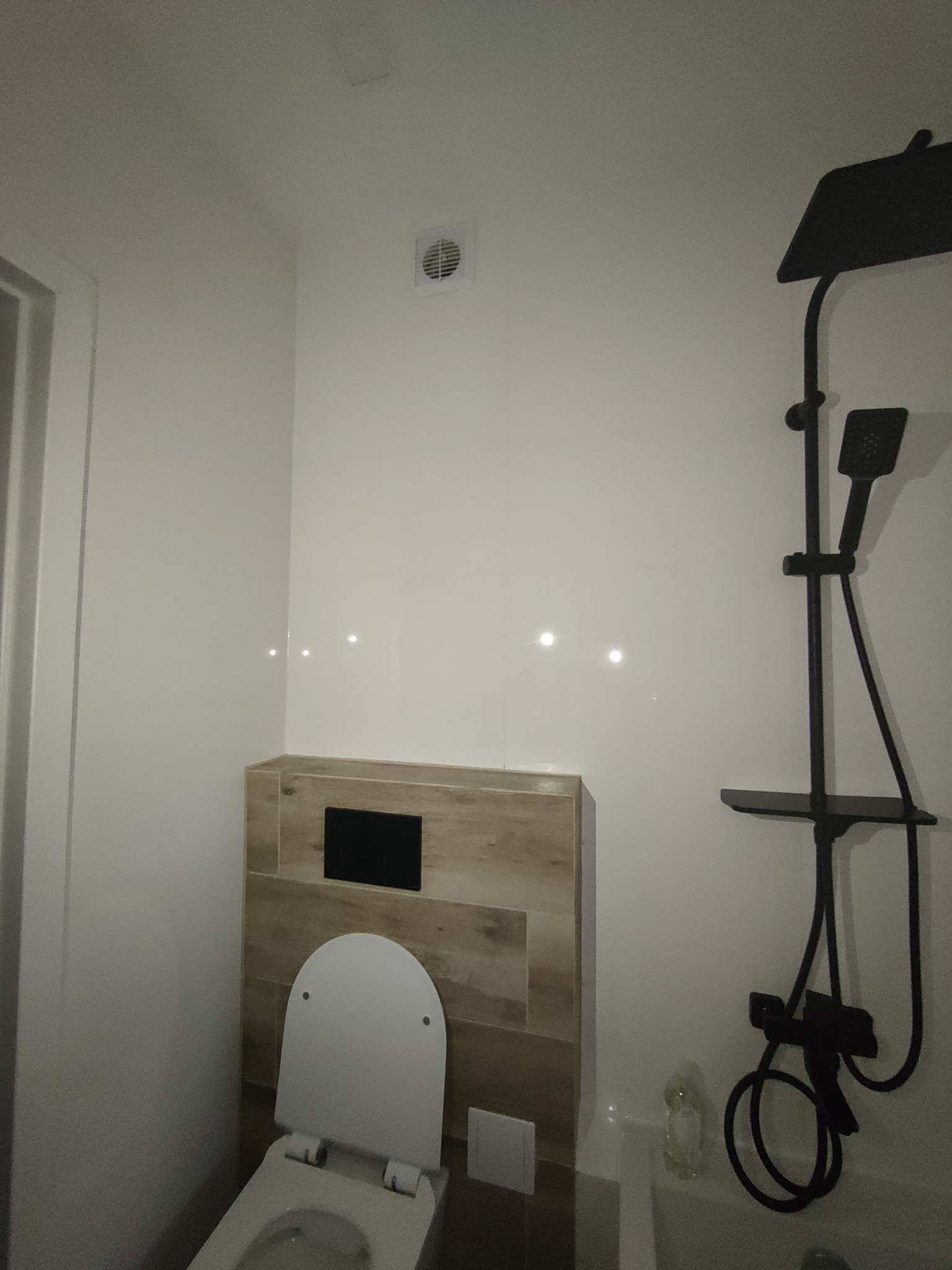 Nowoczesna łazienka z podtynkową toaletą, kabiną prysznicową typu deszczownica w kolorze czarnym i białymi, błyszczącymi płytkami na ścianach.