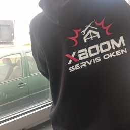 XBOOM SPÓŁKA Z OGRANICZONĄ ODPOWIEDZIALNOŚCIĄ - Pracownik firmy z Bielska-Białej w bluzie z logo 'XBOOM SERWIS OKIEN' stoi przy oknie, na parapecie leżą narzędzia.