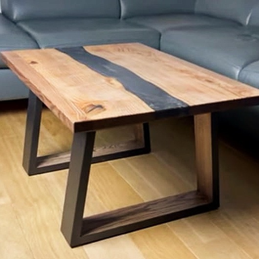 Stolik kawowy z drewnianym blatem z żywicą epoksydową i metalowymi nogami w kształcie litery U, na drewnianej podłodze, z szarą kanapą w tle.