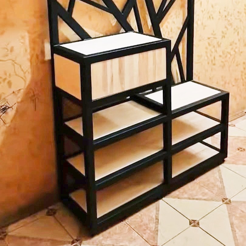 Metalowa konstrukcja z drewnianymi elementami, prawdopodobnie regał lub półka, z geometrycznym wzorem na górze, na tle wzorzystej ściany i podłogi.