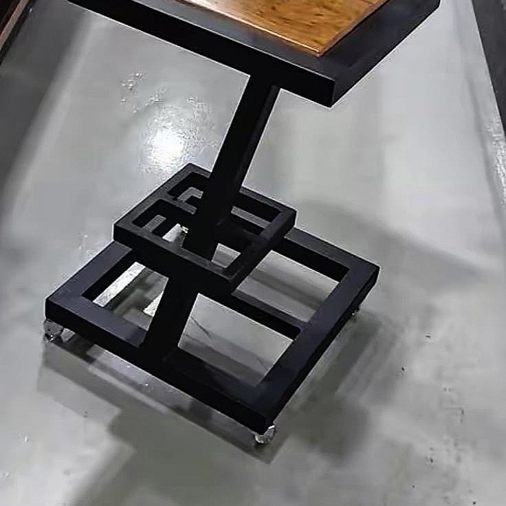 Stolik kawowy z blatem z drewna i geometryczną podstawą z czarnego metalu na kółkach, widok z góry na szarym tle.